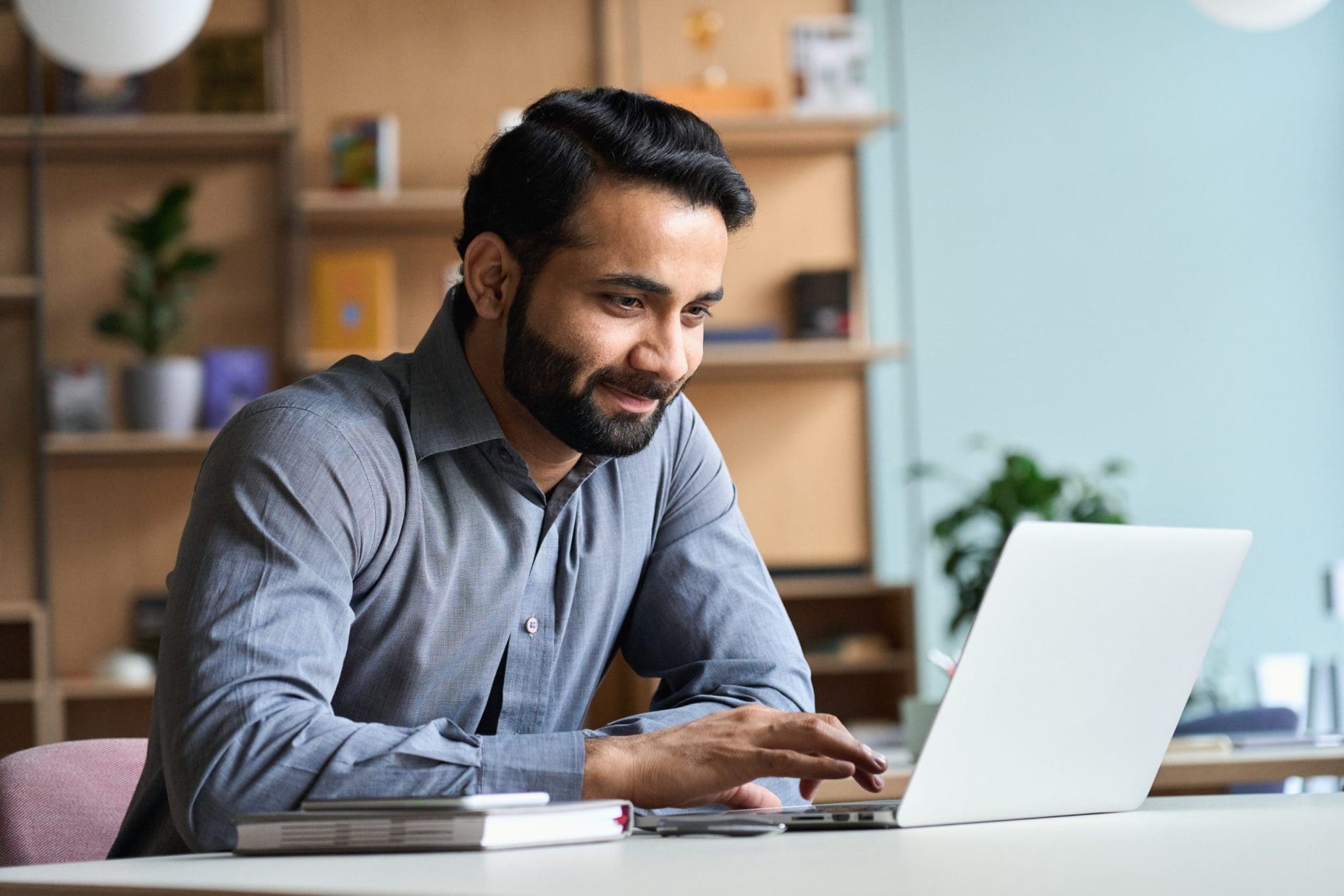 Smiling indian business man working studying on laptop computer at home office.